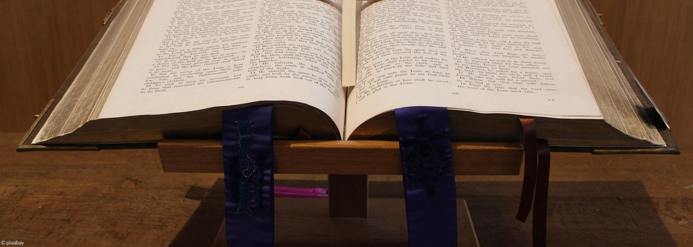 Aufgeschlagene Bibel mit weißem Kreuz in der Mitte aufliegend