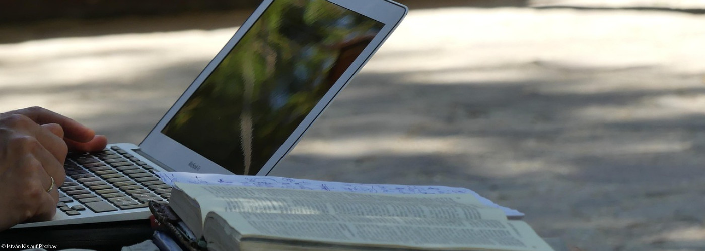 Laptop mit aufgeschlagener Bibel daneben