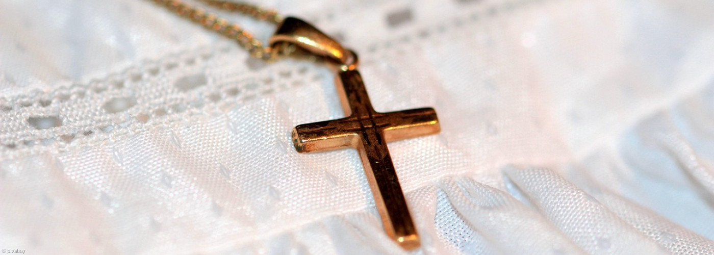 Goldenes Goldkettchen mit Kreuz liegt auf weißem Taufkleid