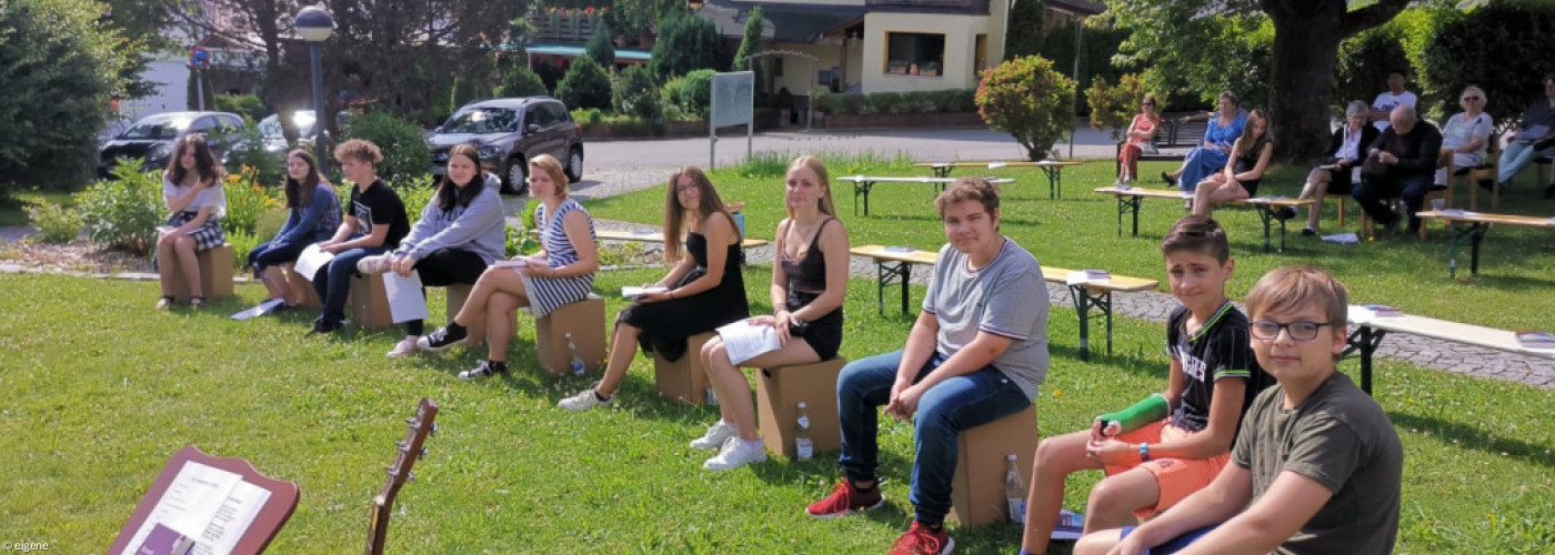 Jugendliche sitzen im Garten nebeneinander, davor Gitarre mit Notenständer