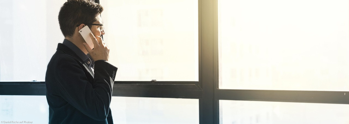 Mann telefoniert vor großem Fenster