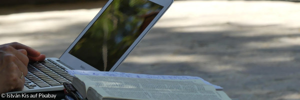 Laptop mit aufgeschlagener Bibel daneben